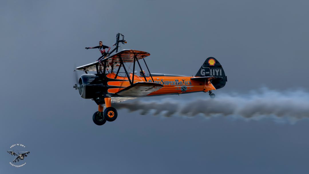 A very orange Boeing Stearman with a passenger on the upper deck.  