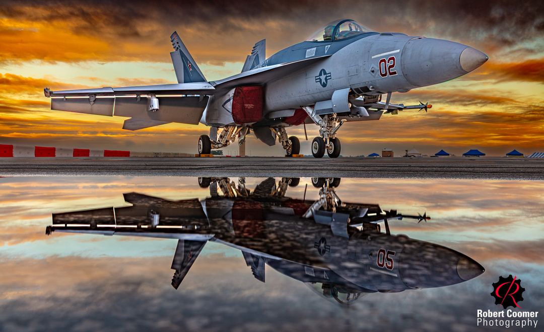 Beauty and the Beast: Morning Aggression

Story: An F/A-18 Aggressor sits on the tarmac at an airshow after a morning storm. This deadly weapon lulls you into a false sense of serenity, bathed in warm morning light and reflected in the rain-soaked pavement. The image is an HDR composite of five exposures.

Intention: To create a beauty shot of this aggressive beast, posing like a supermodel, but a very deadly one at that…

Attention: The brilliant morning light draws your eye into the frame and toward the body of the jet.

Captivation: Your eye then drops to the reflection, where the smooth, beautiful aircraft becomes fractured and distorted by the water. There's something unsettling about that contrast.