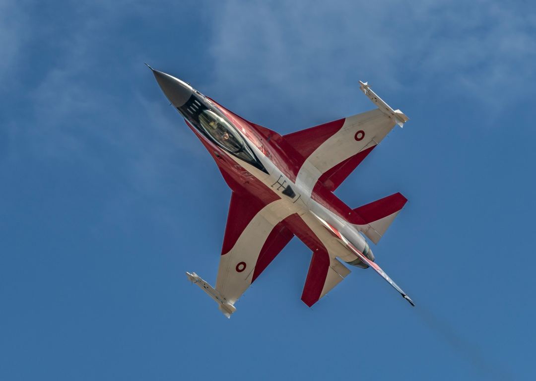 F‑16 Dannebrog soars through a clear blue sky, proudly displaying its striking special livery inspired by Denmark’s national flag.