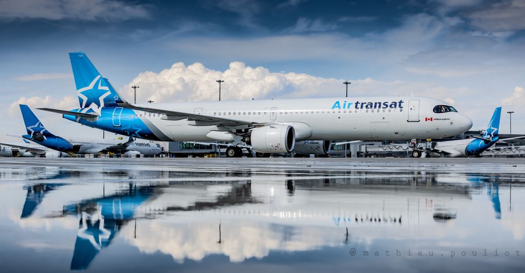 An other day, an other puddle... a recent downpour made the tarmac extra reflective as this Air Transat A321 was taxiing in. In the background, two Air Transat A330s are seen parked at the main terminal.