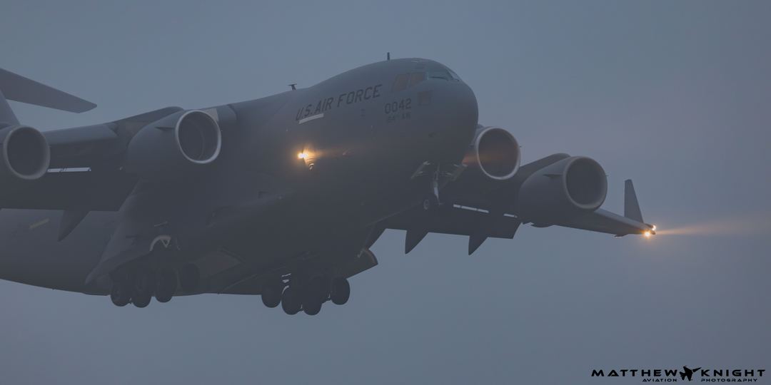 At about half 6 in the morning at RAF Lakenheath I took this shot of a C-17 Globemaster breaking through the clouds.

Not long before another had landed but didn't see it, I heard it though!

I love the lights producing a beam because of the fog.