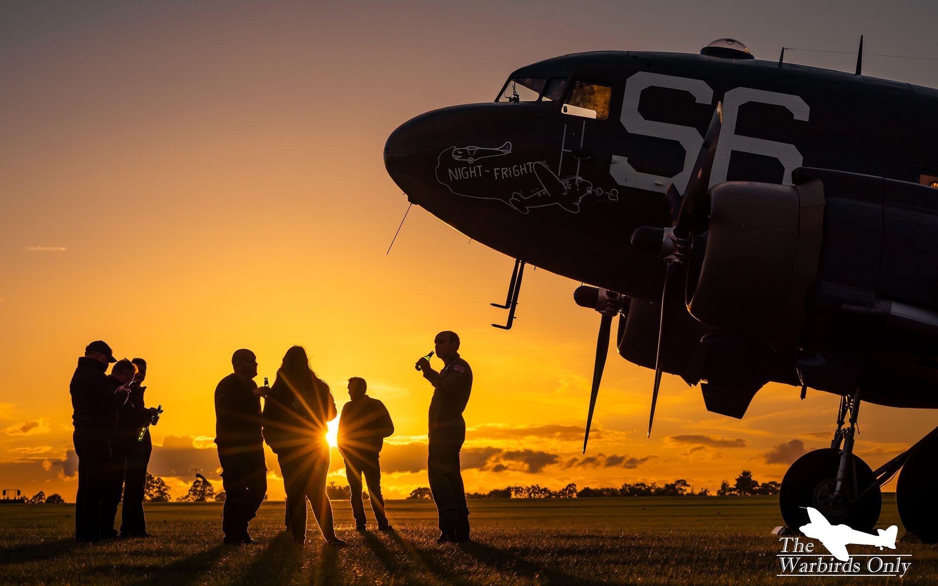 A C-47 Skytrain parked at Sywell at sunset, with a group of people silhouetted beside it