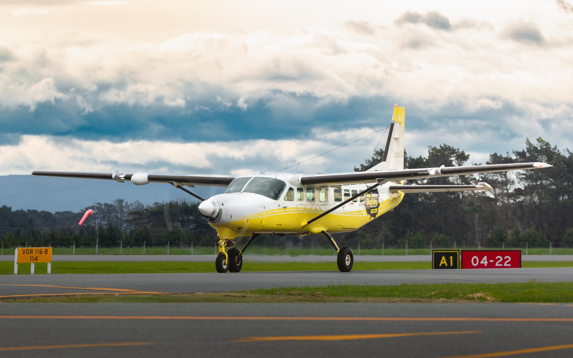 A yellow and white single-engine turboprop on a taxiway under a heavy, cloudy sky.