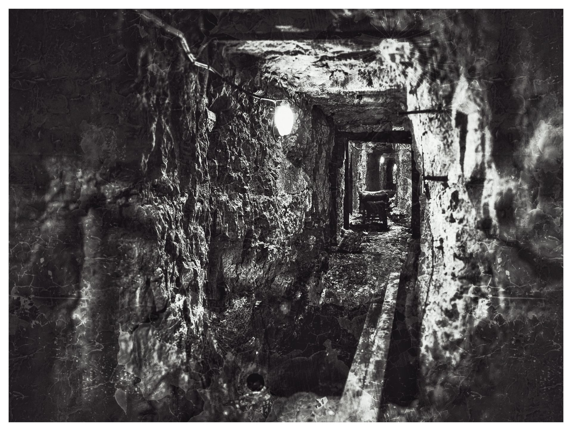 A black and white shot down a narrow rock tunnel in the Ypres caves, lit by bare bulbs