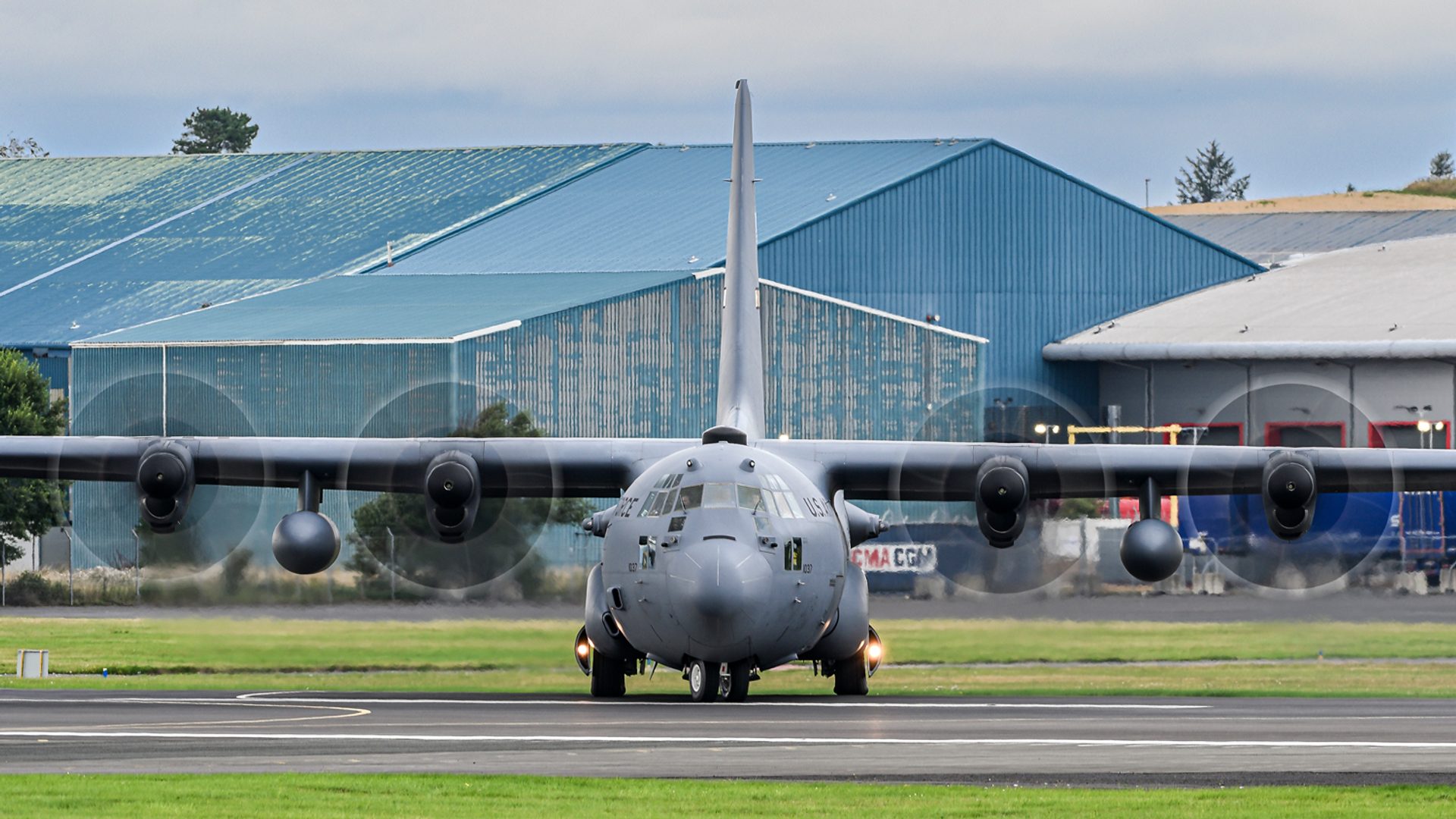 A C-130 Hercules seen head on as it turns onto the runway, all four propellers blurred into discs.