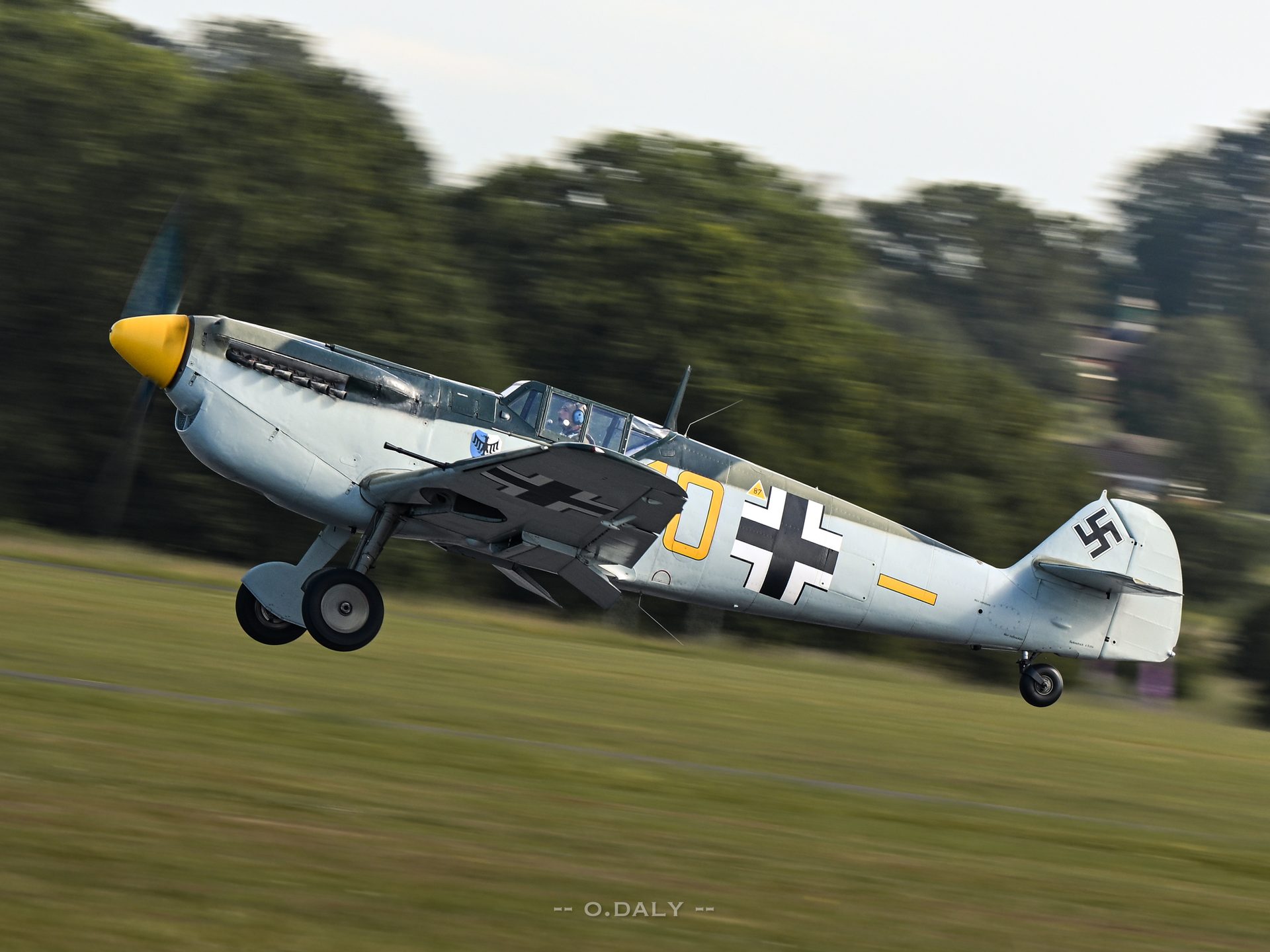 A Bf 109 lifting off at Cosford, its propeller blades blurred and the airframe sharp against streaked trees.