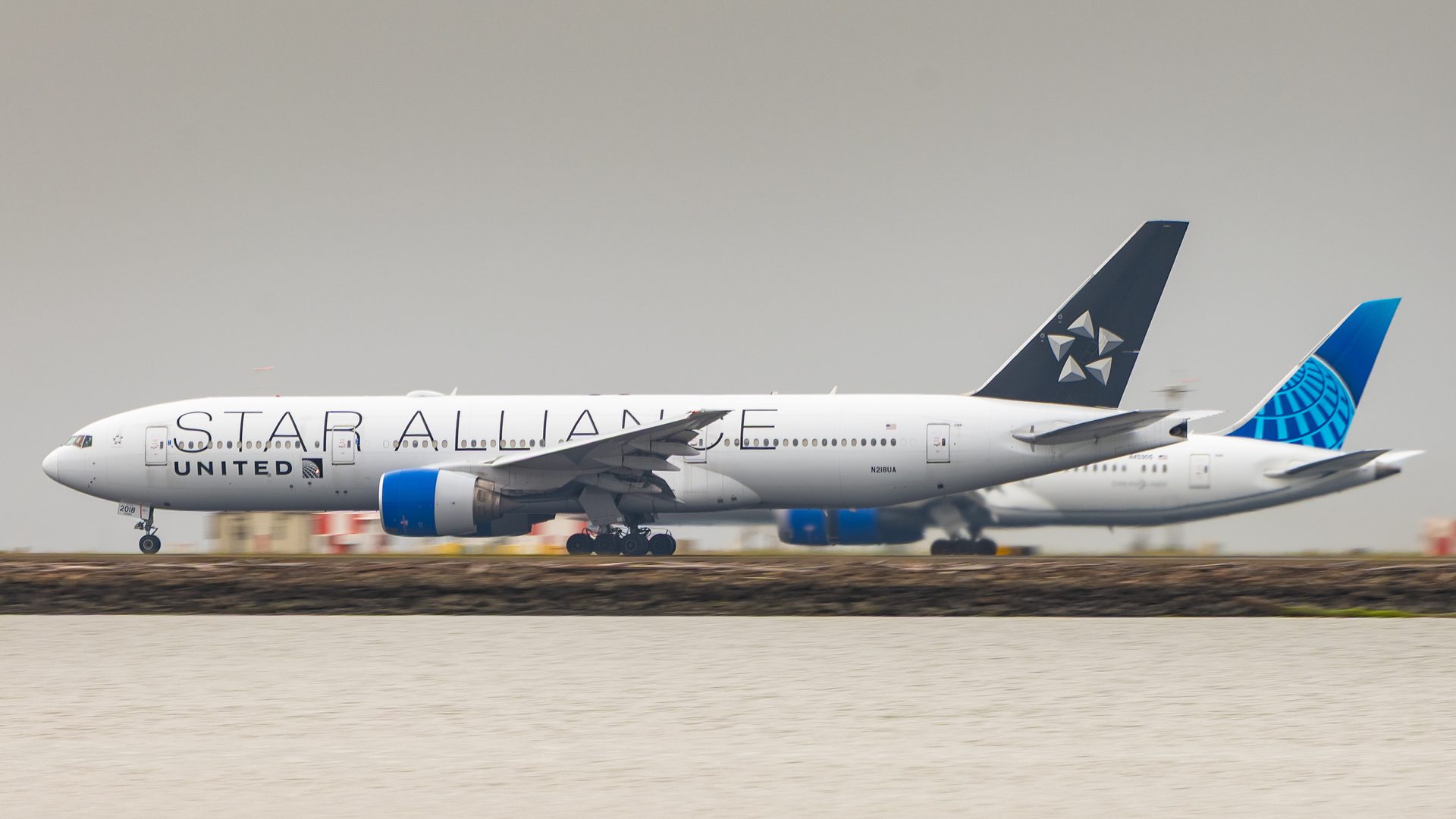 Two United airliners side by side on parallel runways at San Francisco, one in Star Alliance colours, with water in the foreground.