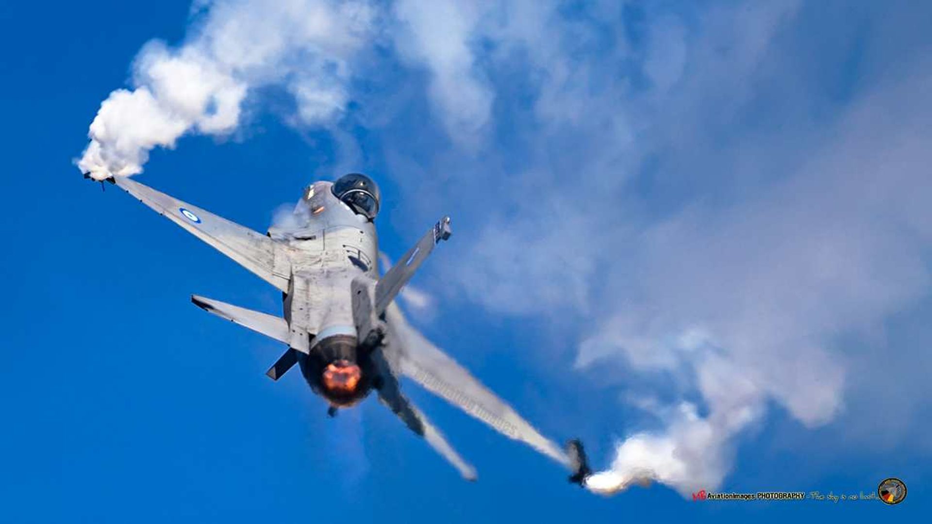 An F-16 pulling up through a display at Belgian Air Force Days at Florennes, afterburner lit and smoke trailing from its wingtips against a blue sky