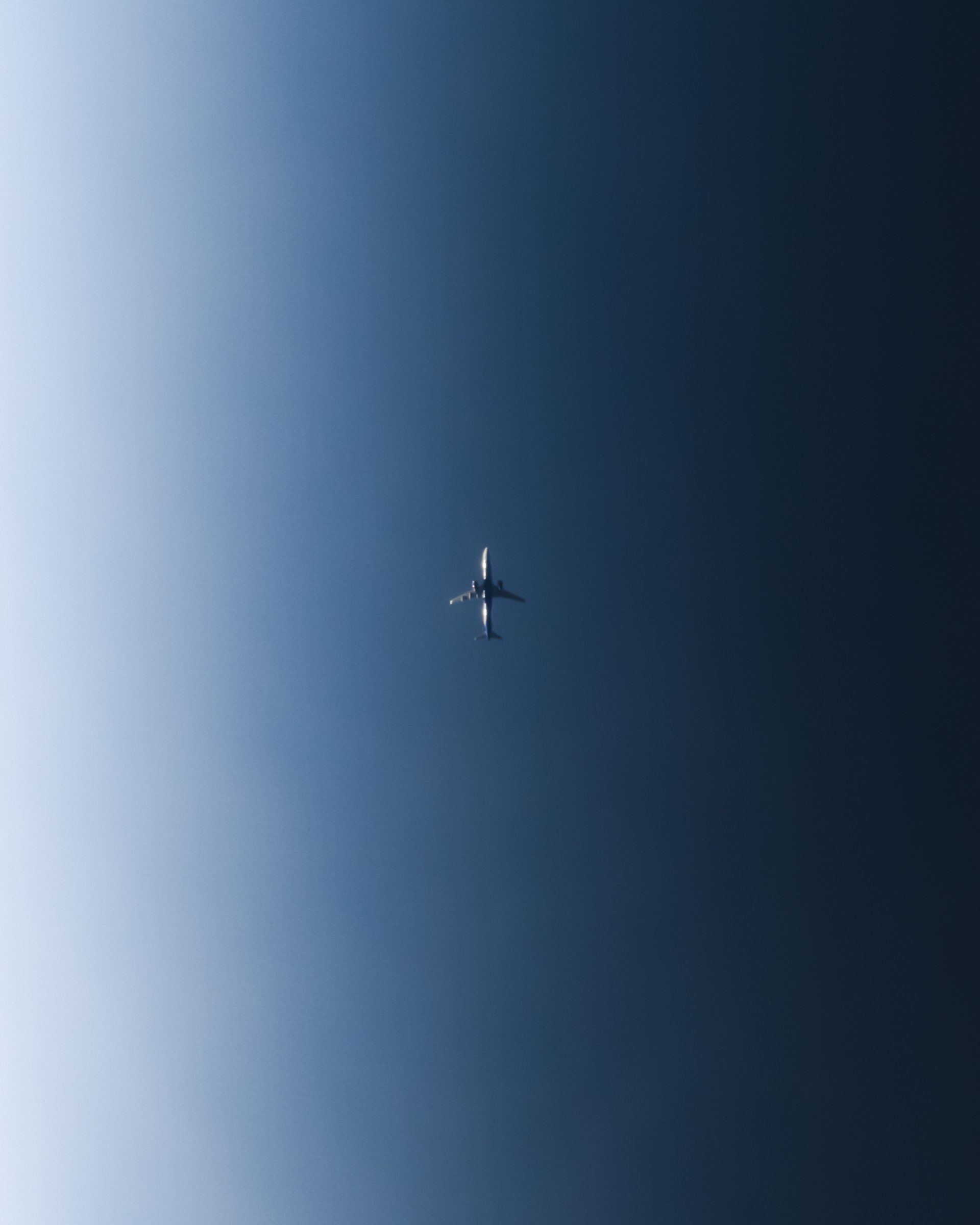 An airliner small in the middle of a blue gradient sky, with most of the shot left empty.