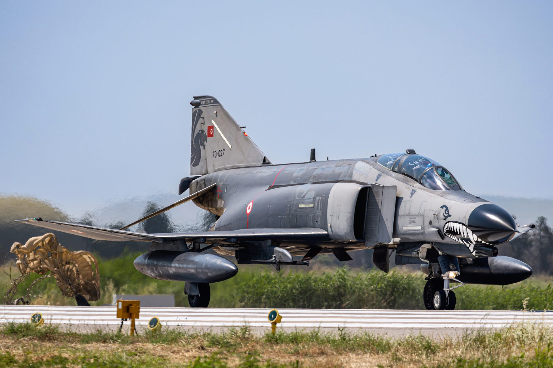 A grey Turkish Air Force F-4 Phantom II with a shark mouth on its nose, rolling along the runway with its drag chute behind it