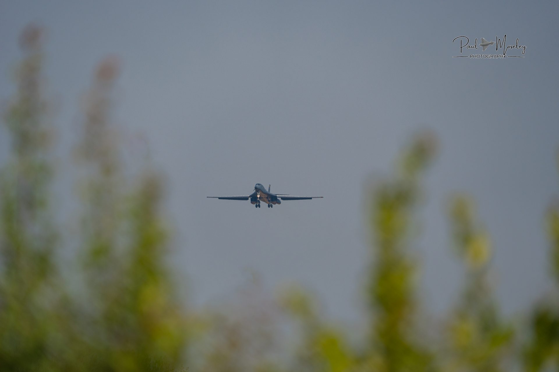 A B-1 Lancer arriving at RAF Fairford, seen through bushes