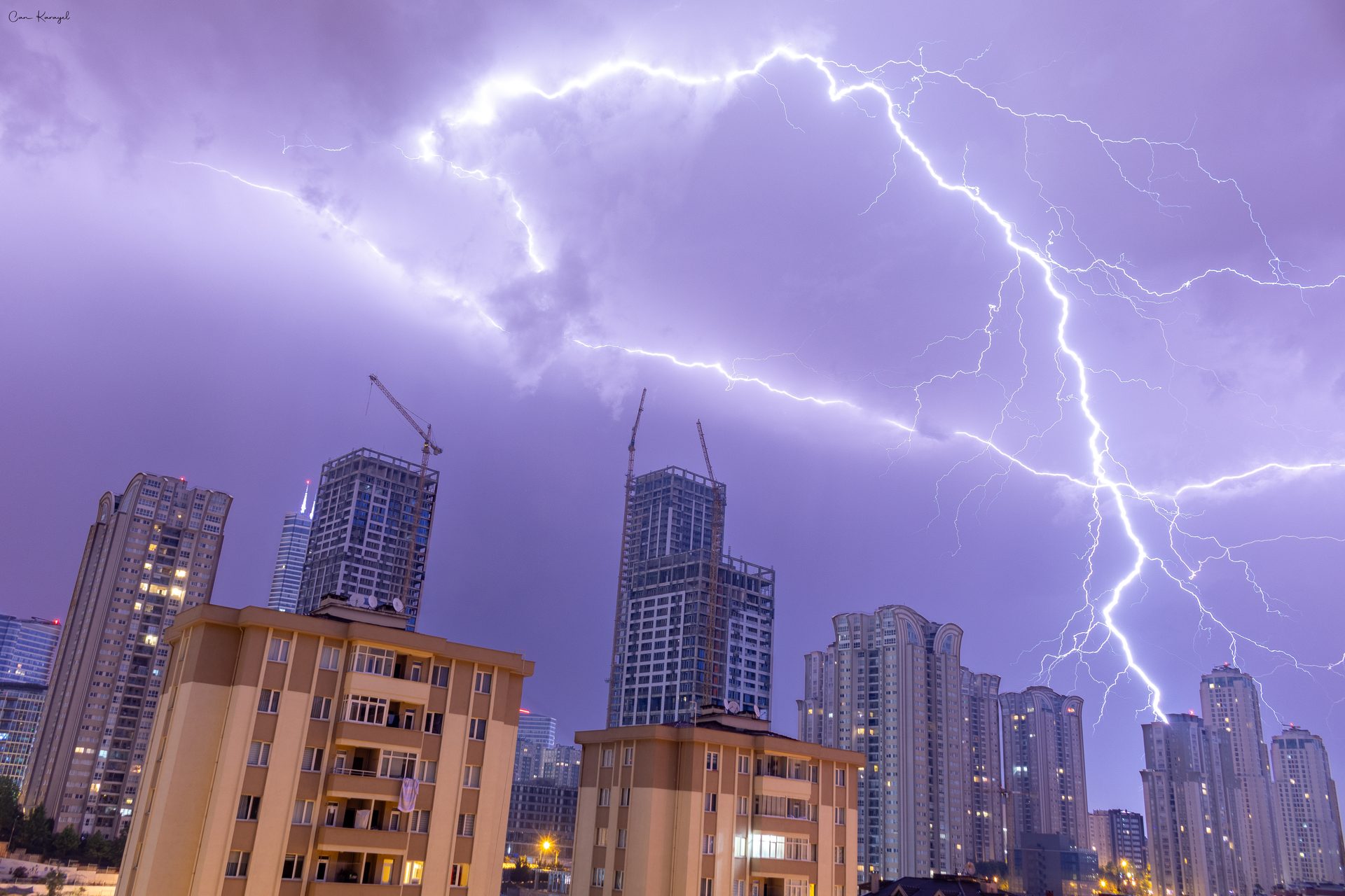 Forks of lightning across a purple night sky over tower blocks and cranes in Istanbul